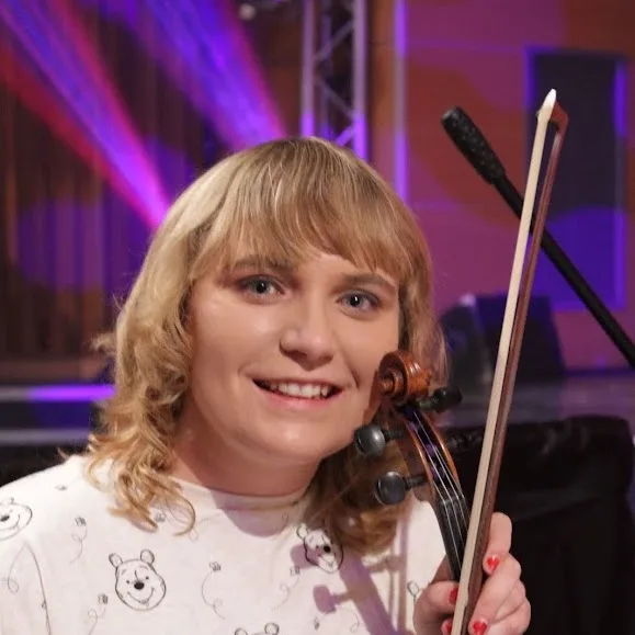 Caitlin smiling, holding her violin and bow